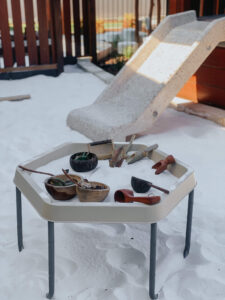 Table containing gardening things placed at white sand besides marble slide