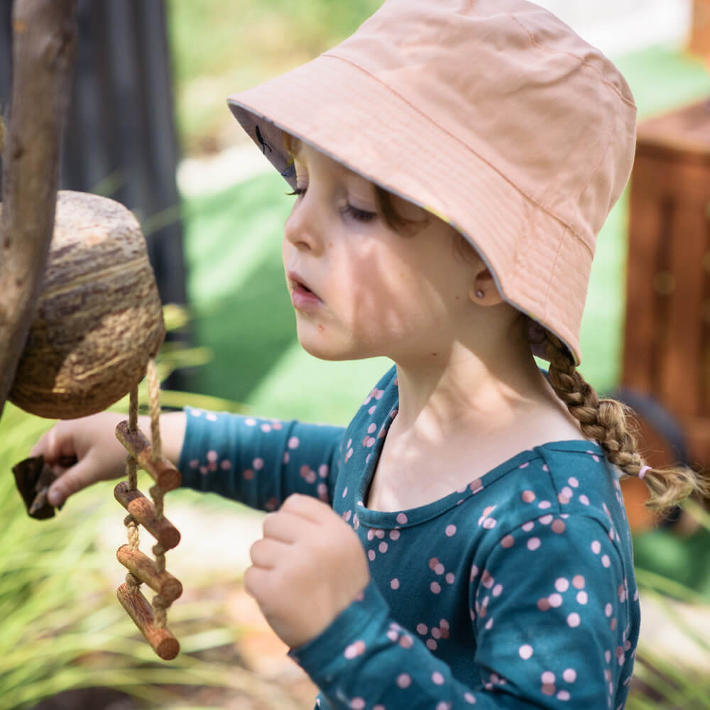 Child looking into hanging coconut cage bird house at nido early school